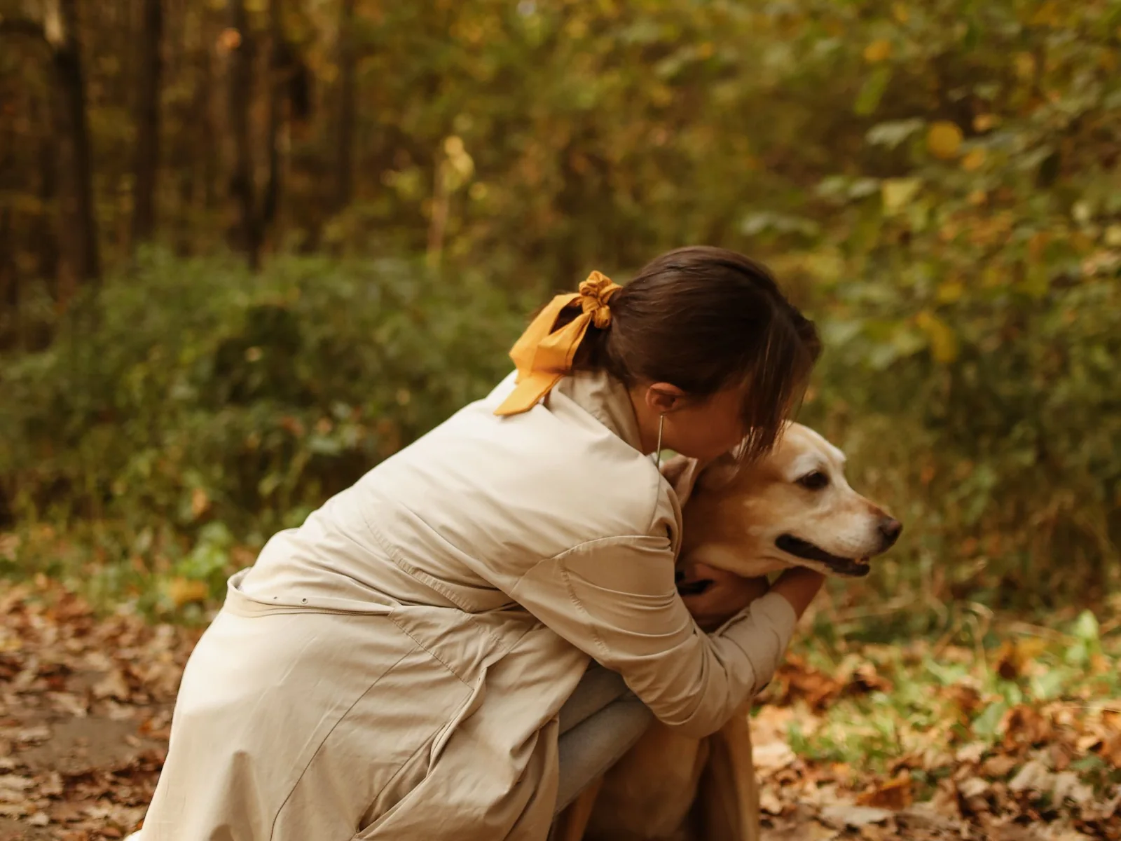A woman crouched in autumn leaves, hugging her labrador