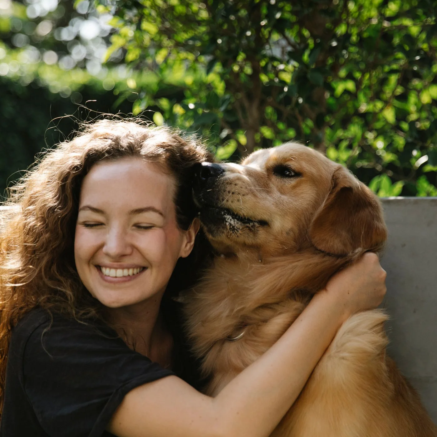 A smiling woman hugging her golden retriever in the garden